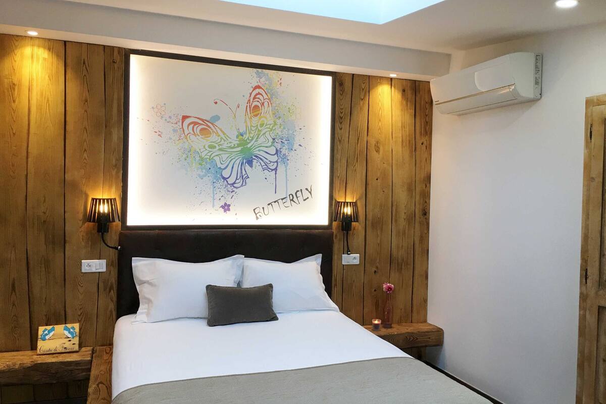 A bedroom with a wooden headboard, a bed with white bedding, two wall-mounted lamps, and a ceiling skylight.