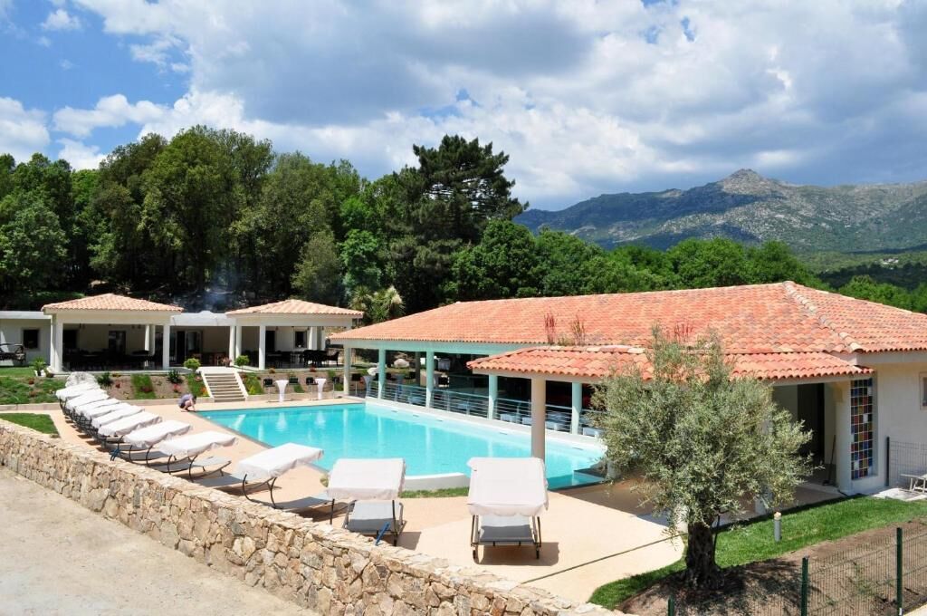 A pool area with lounge chairs and a building with a tiled roof.