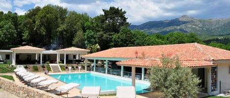 A pool area with lounge chairs and a building with a tiled roof.