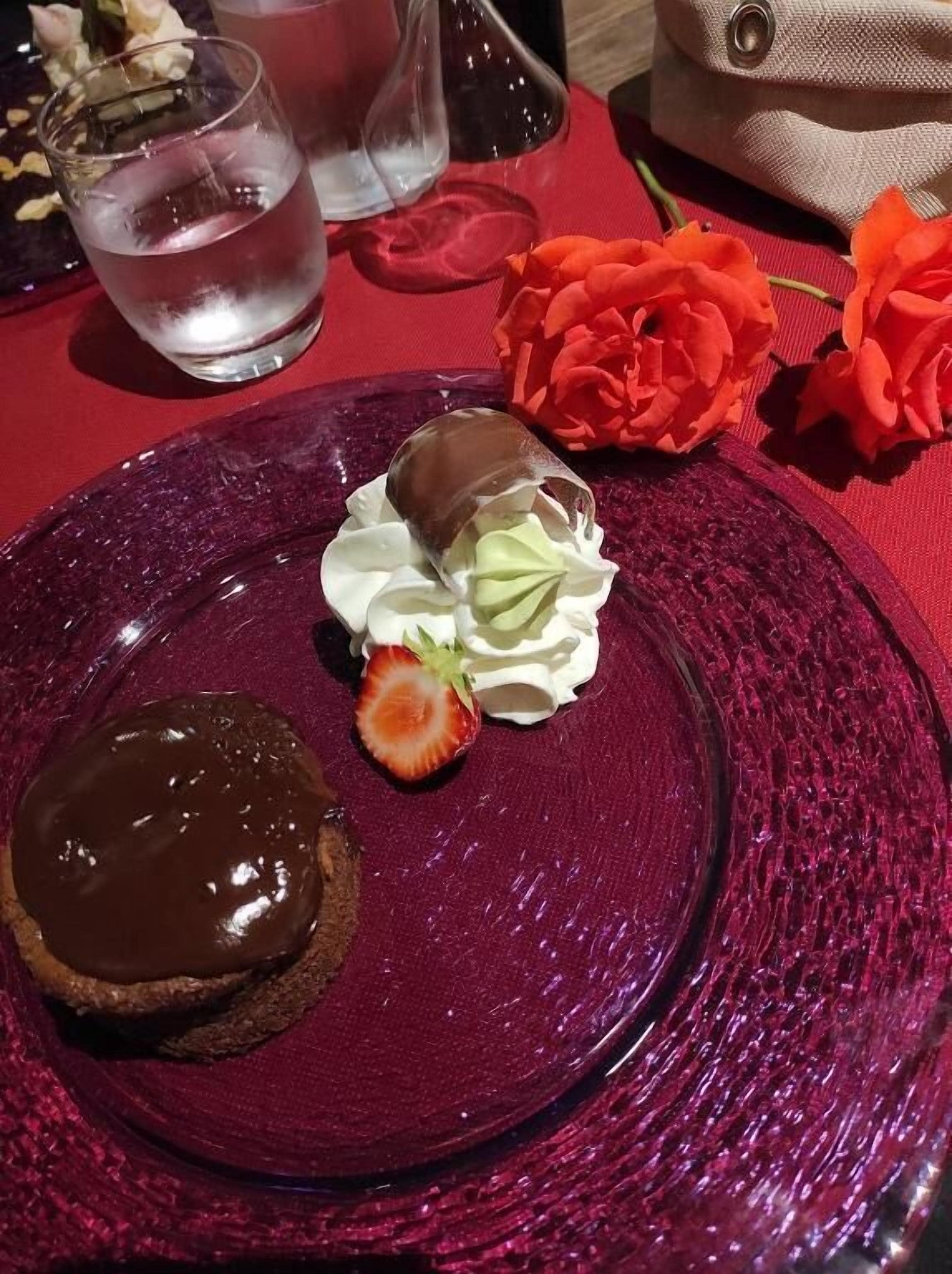 A dessert plate with a chocolate-covered pastry, a strawberry, and whipped cream.