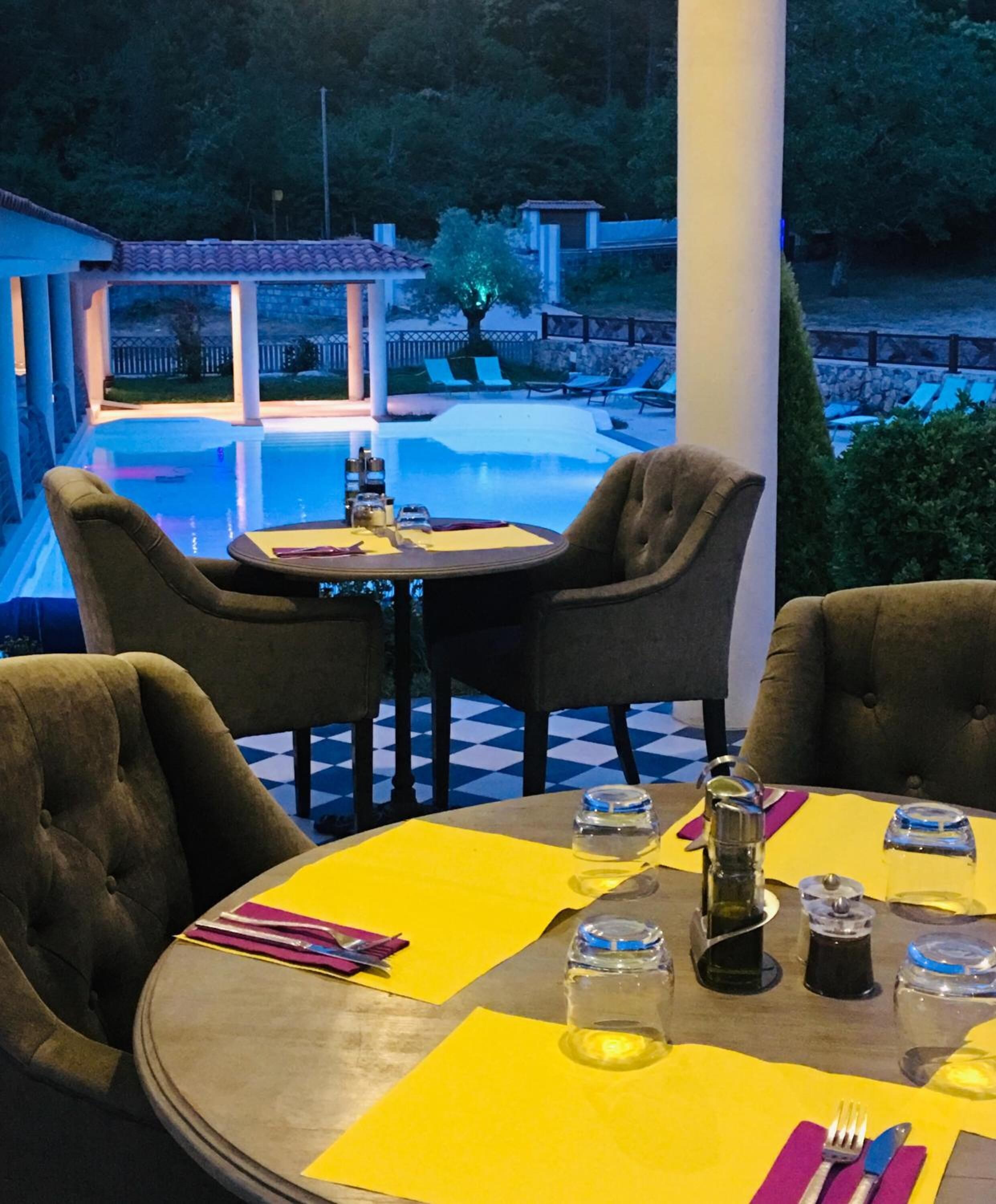 Een terras met eethoek en uitzicht op een zwembad, met ronde tafels en stoelen, en een sfeervolle verlichting.