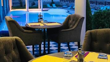 Een terras met eethoek en uitzicht op een zwembad, met ronde tafels en stoelen, en een sfeervolle verlichting.