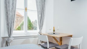 A bedroom with a bed, a window with curtains, a table with a bottle and glasses, and two chairs. - Old Town Tale Apartments (Zagreb)