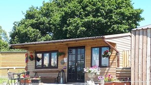 A wooden building with a porch, large windows, and flower pots. - Rosie Traditional Gypsy Wagon (Rhayader)