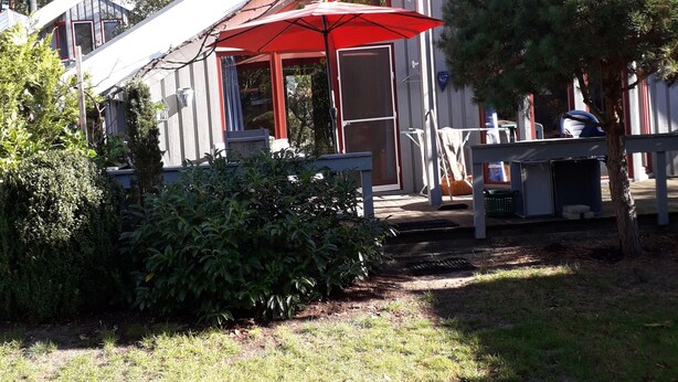 Une maison avec un parapluie rouge, un petit porche et un jardin.