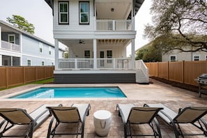 Ein zweistöckiges Haus mit überdachter Terrasse, Swimmingpool und Sitzgelegenheit im Freien.