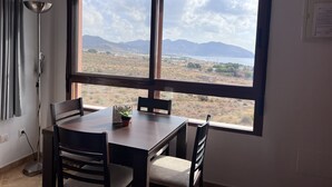 Een eethoek met een tafel en stoelen, een potplant, een lamp en uitzicht op een landschap met bergen en een waterlichaam.