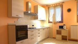 A compact kitchen with a stove, oven, and microwave, light-colored cabinets, and a window with curtains. - Autumn Apartment (Agriturismo Il Melograno) (Venezia)