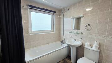 Een badkamer met een bad, wastafel, toilet en een raam.