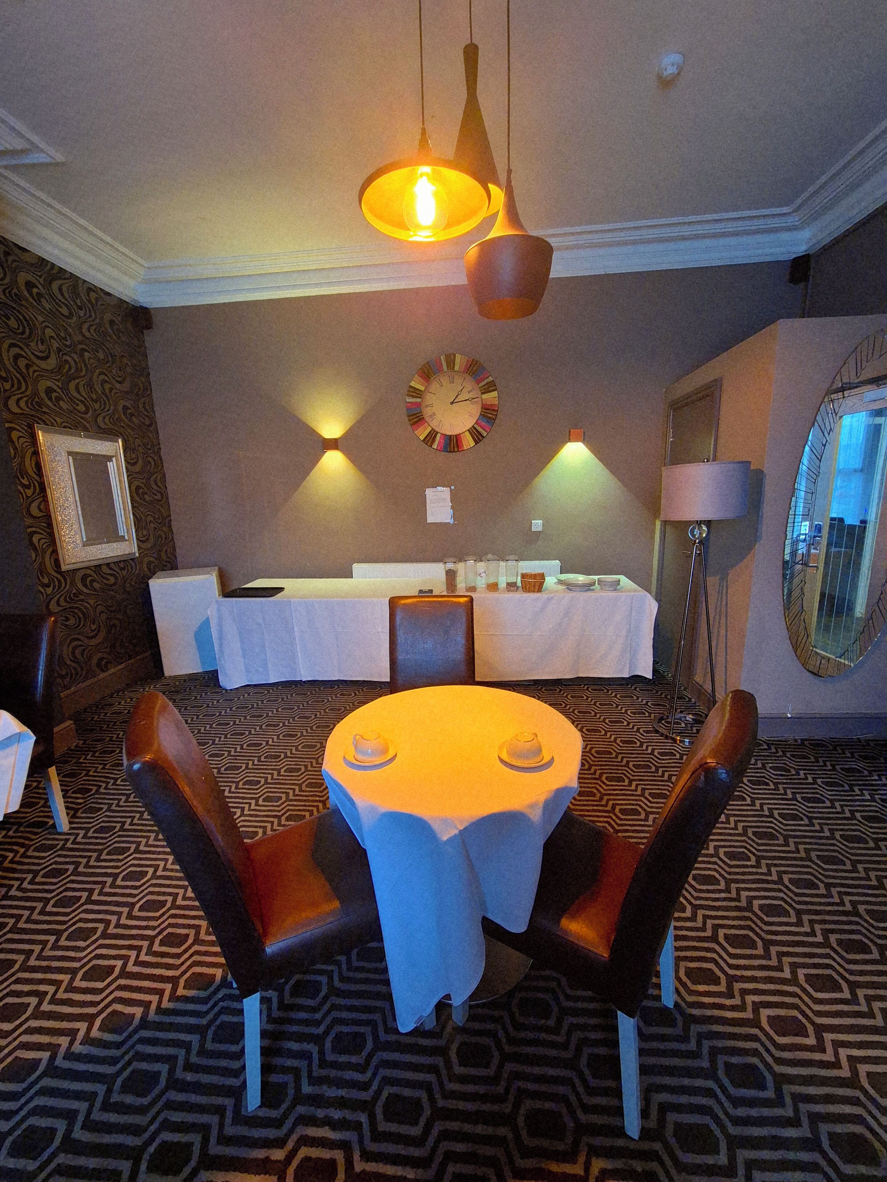 A dining area with a round table, chairs, a clock, and a patterned carpet.