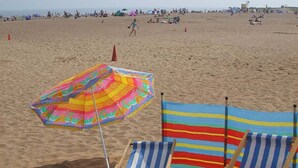 A beach with two striped beach chairs and a colorful umbrella. - OYO Ivy Hotel (Skegness)