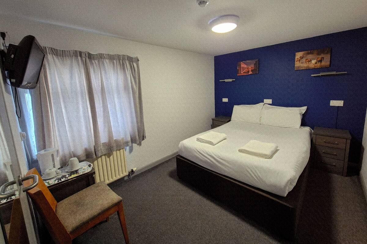 A hotel room with a bed, a chair, a desk with a computer, and a window with curtains.