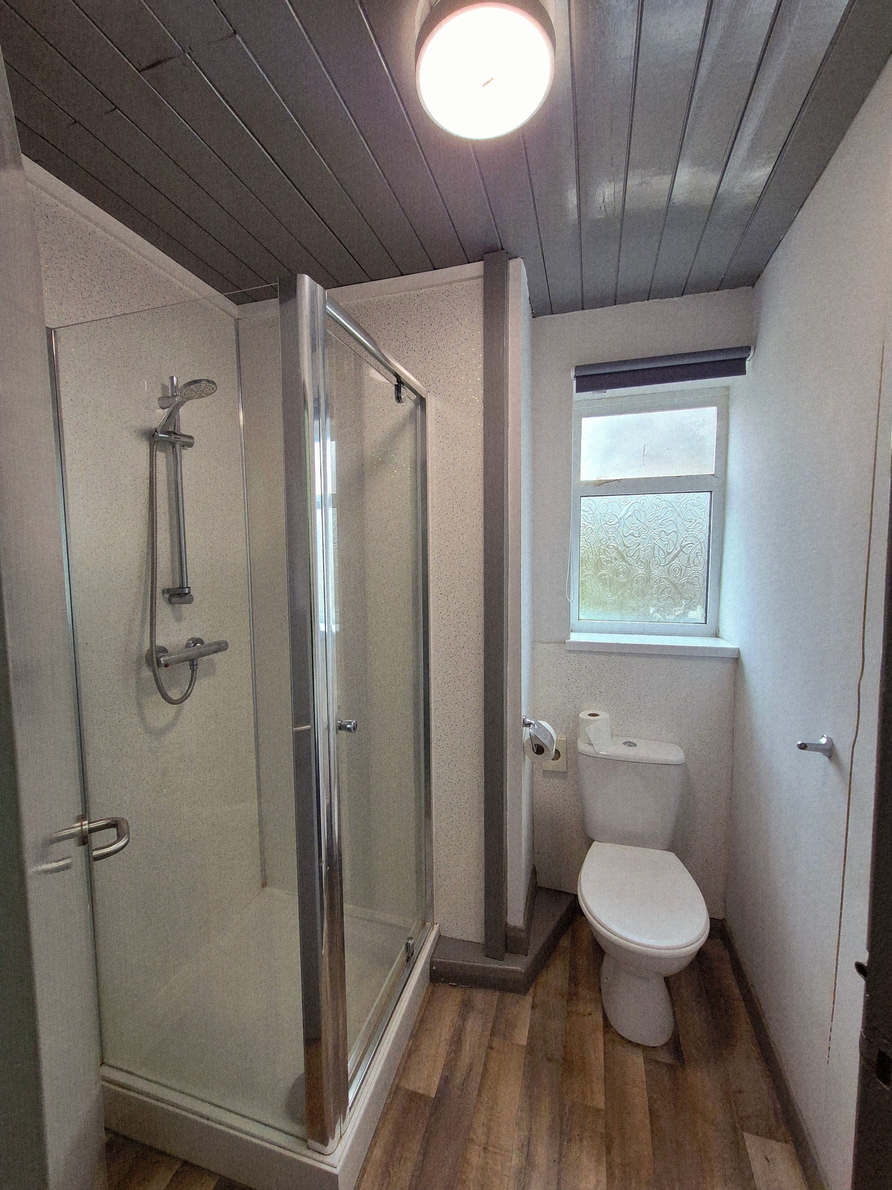 Une petite salle de bain avec une douche à parois de verre, des toilettes et une fenêtre.