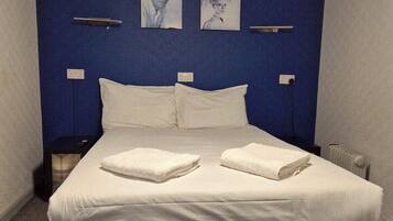 A neatly made bed with white linens and two towels, a bedside table, a nightstand, and two wall-mounted light fixtures.