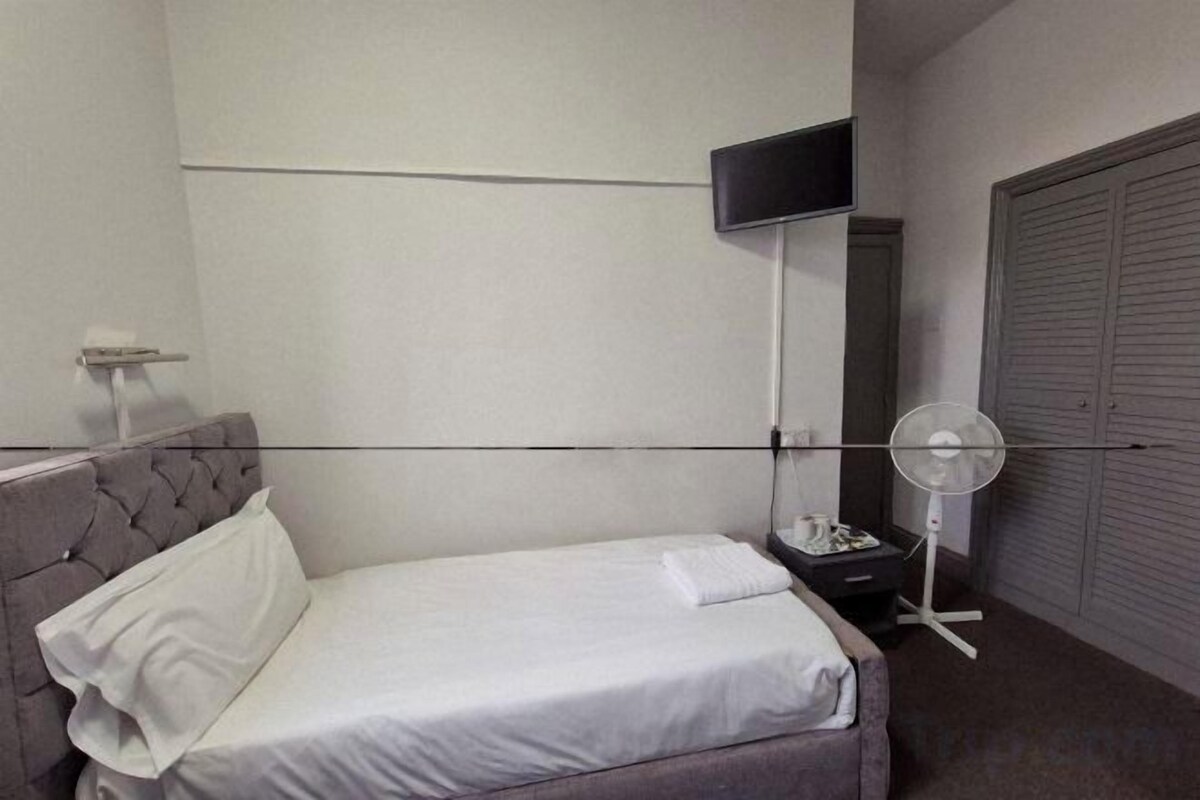 A hotel room with a bed, a flat-screen TV mounted on the wall, a bedside table with a lamp, and a closet with sliding doors.