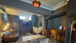A modern interior with a patterned floor, a leather sofa, a dining table with chairs, and a bar area with a cushioned chair. - OYO Ivy Hotel (Skegness)