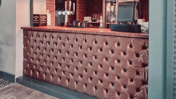A bar area with a tufted leather counter, pendant lighting, and a large mirror reflecting the interior. - OYO Ivy Hotel (Skegness)