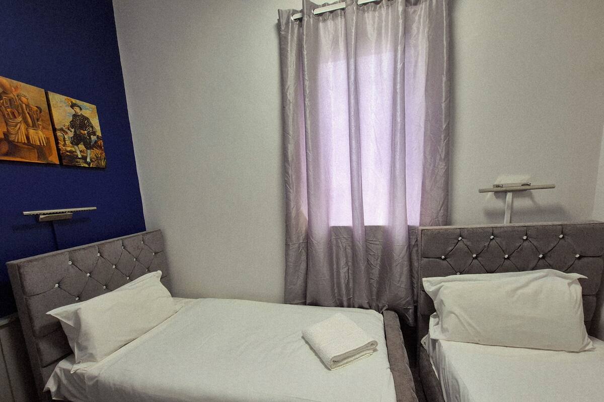 A hotel room with two beds, a blue accent wall, and a window with sheer curtains.