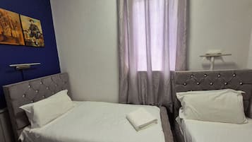 A hotel room with two beds, a blue accent wall, and a window with sheer curtains.