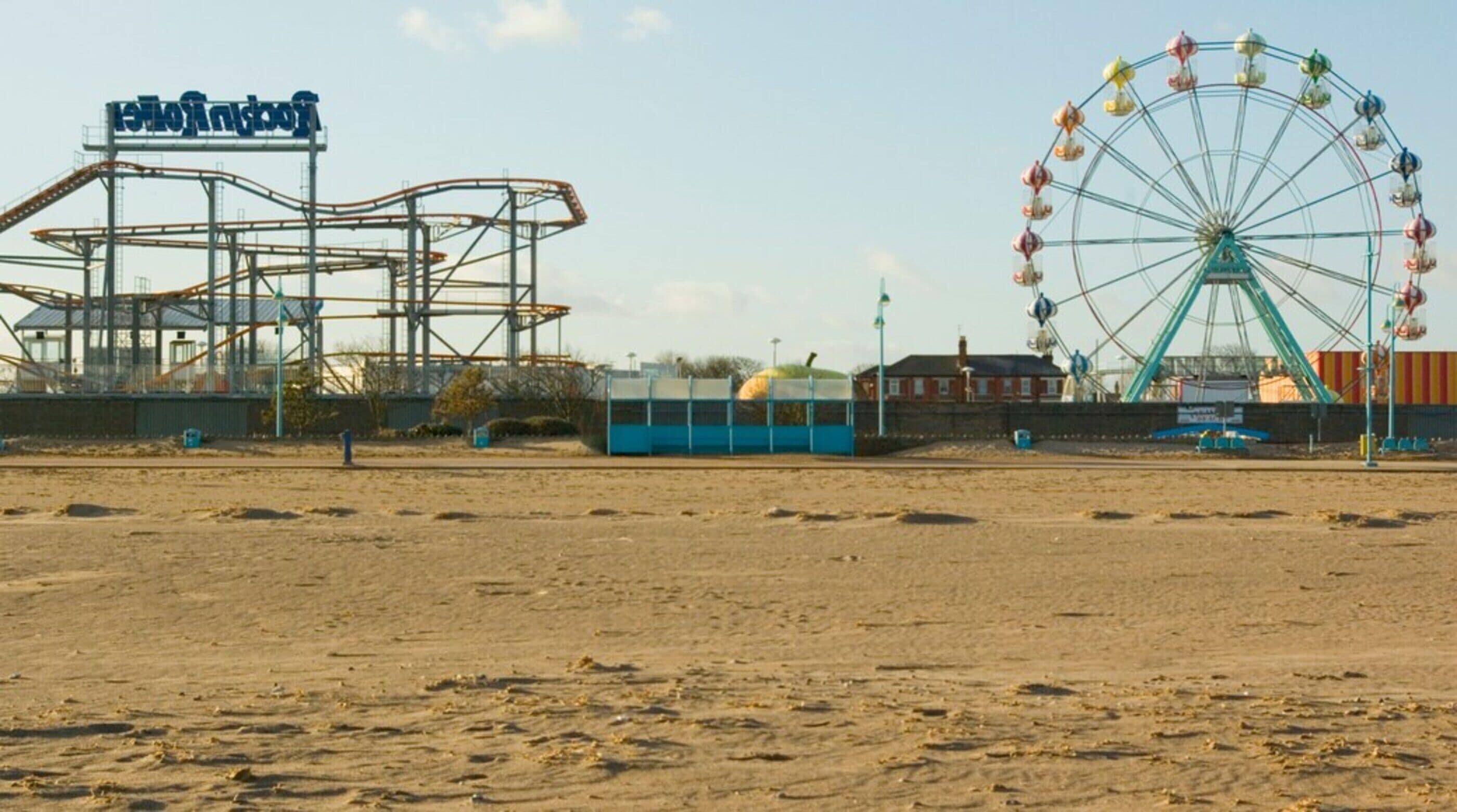Ein Strand mit Achterbahn, Riesenrad und einem Gebäude mit Schilder.