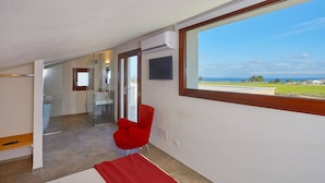 Une salle de bain moderne avec une douche à l’italienne en verre, une chaise rouge et une grande fenêtre donnant sur la mer.