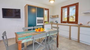 Une cuisine moderne dotée d’un four encastré, d’une table à manger avec des chaises et d’une fenêtre donnant sur des palmiers.