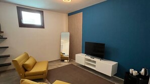Un salon avec un canapé, un téléviseur, une table basse et une fenêtre.