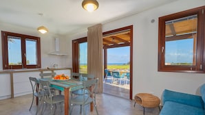 Un vaste espace de vie comprenant une table à manger, des chaises et un canapé bleu. De grandes fenêtres offrent une vue sur l’extérieur.