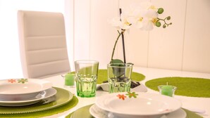 A dining table set with green placemats, white plates, and clear glassware. - Apartments Green Paradise D&S (Bohinj)
