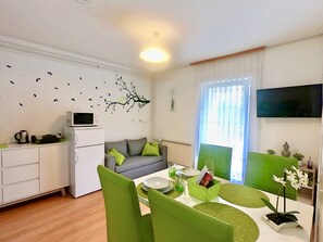 A modern living room with a sofa, dining table, chairs, a flat-screen TV, and a decorative wall.