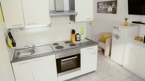 A modern kitchen with white cabinets, a stainless steel sink, a built-in oven, and a flat-screen TV mounted above the counter. - Apartments Green Paradise D&S (Bohinj)