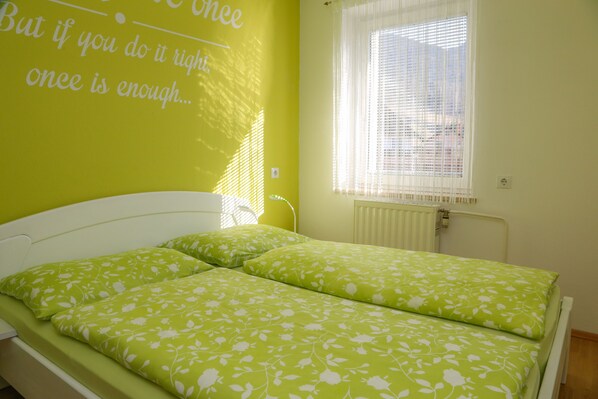 Una habitación con cama, ventana con persianas y una pared con una cita inspiradora.