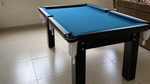 A pool table in a room with tiled flooring, windows with bars, and a couch with a striped pillow. - Pousada universitária (Teresina)