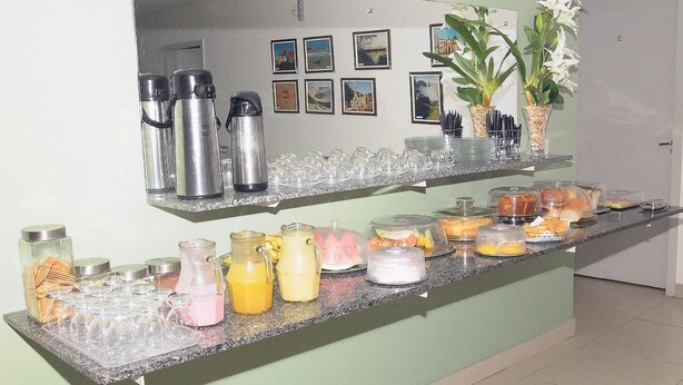 A buffet counter with various food and drink options, including jars of snacks, pitchers of beverages, and covered dishes. - Pousada universitária (Teresina)