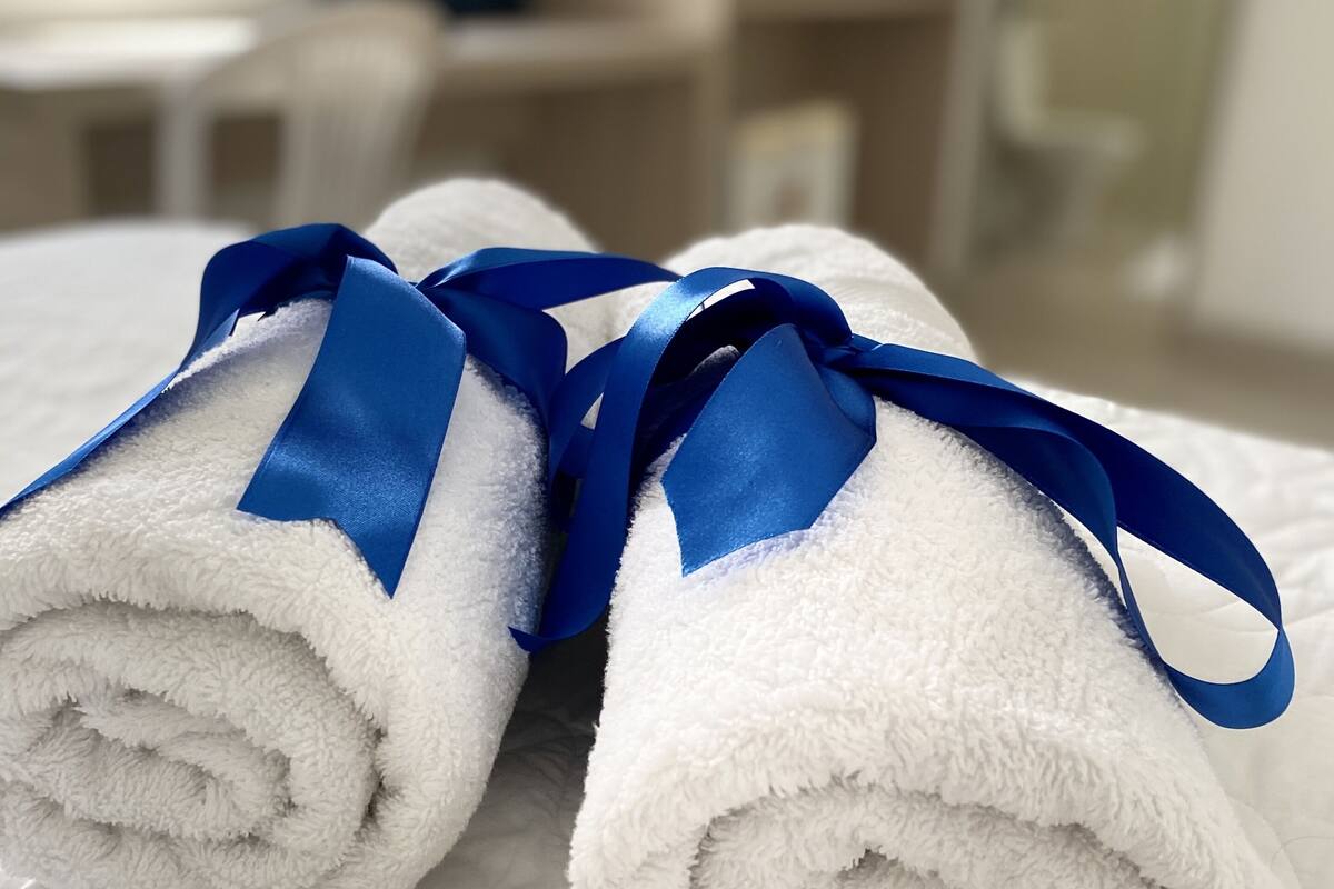 Duas toalhas brancas com fitas azuis amarradas, sobre uma cama num quarto de hotel.