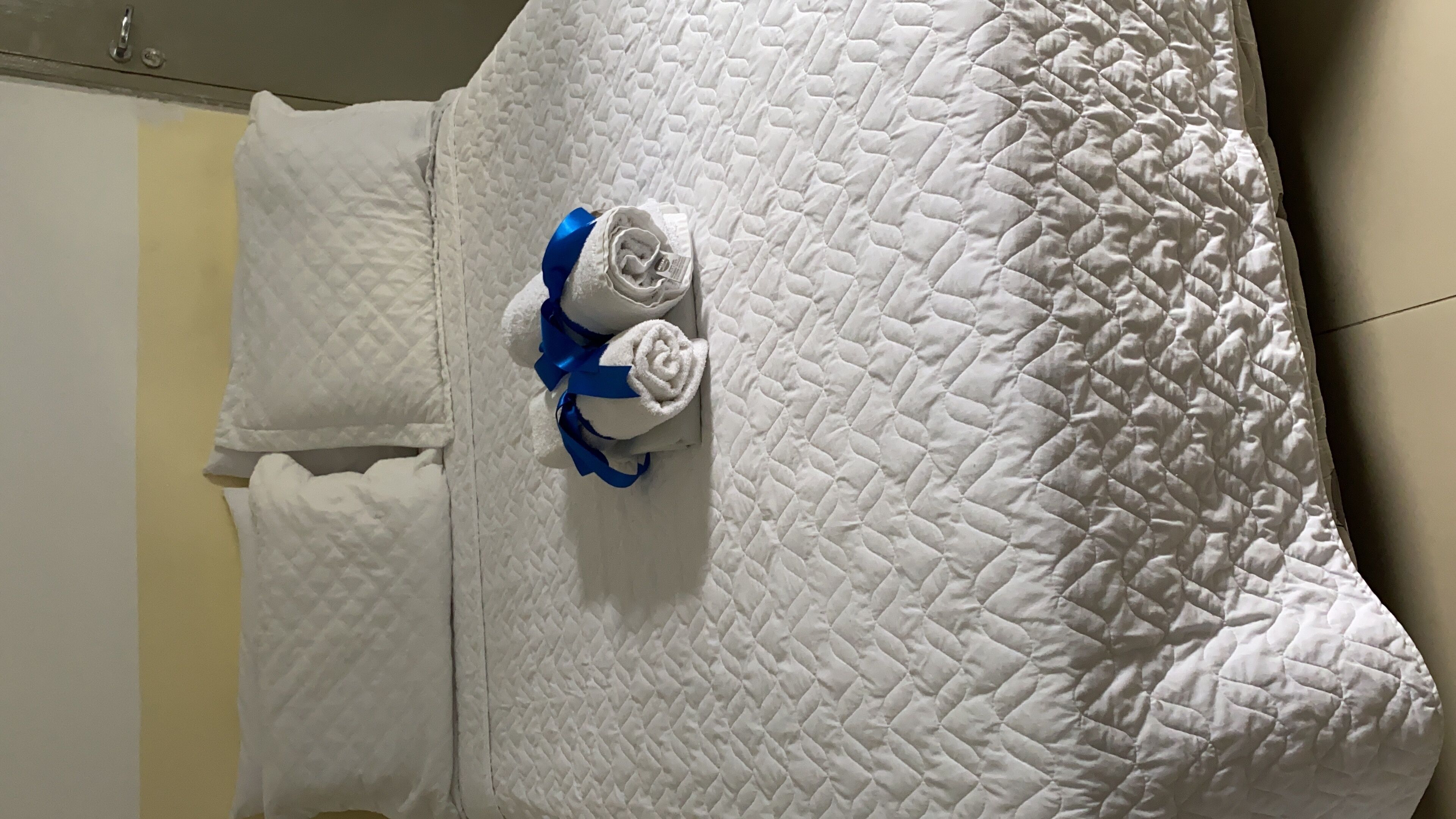 Un lit blanc matelassé, orné d’un ruban bleu noué autour de la tête de lit.