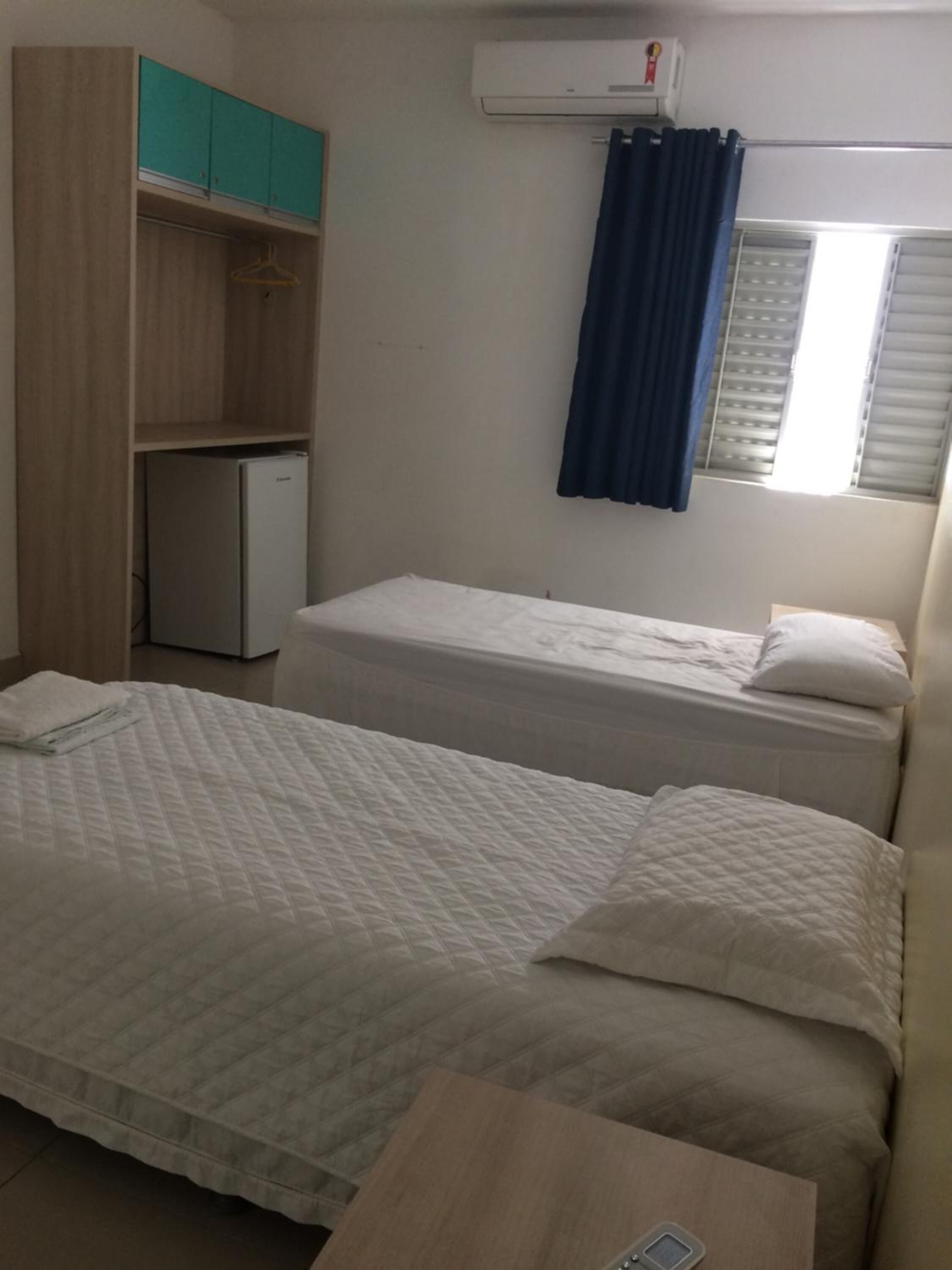 Een kamer met twee bedden, een kleine koelkast, een kledingkast en een airconditioning.
