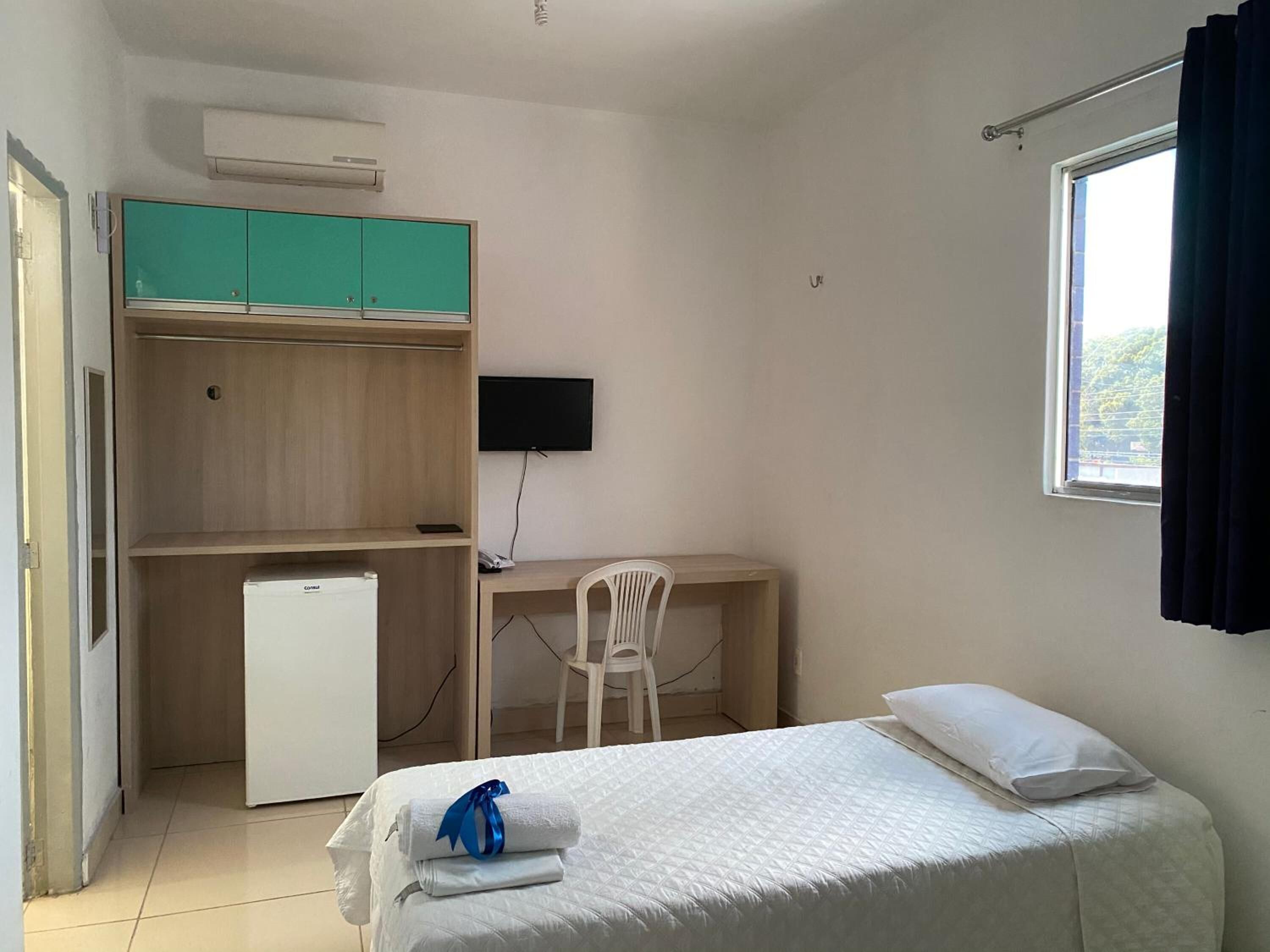 A compact hotel room with a bed, a desk with a chair, a TV, and a wardrobe.