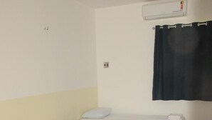A hotel room with three single beds, each with a white bedspread and pillows, a dark curtain, and a wall-mounted air conditioning unit. - Pousada universitária (Teresina)