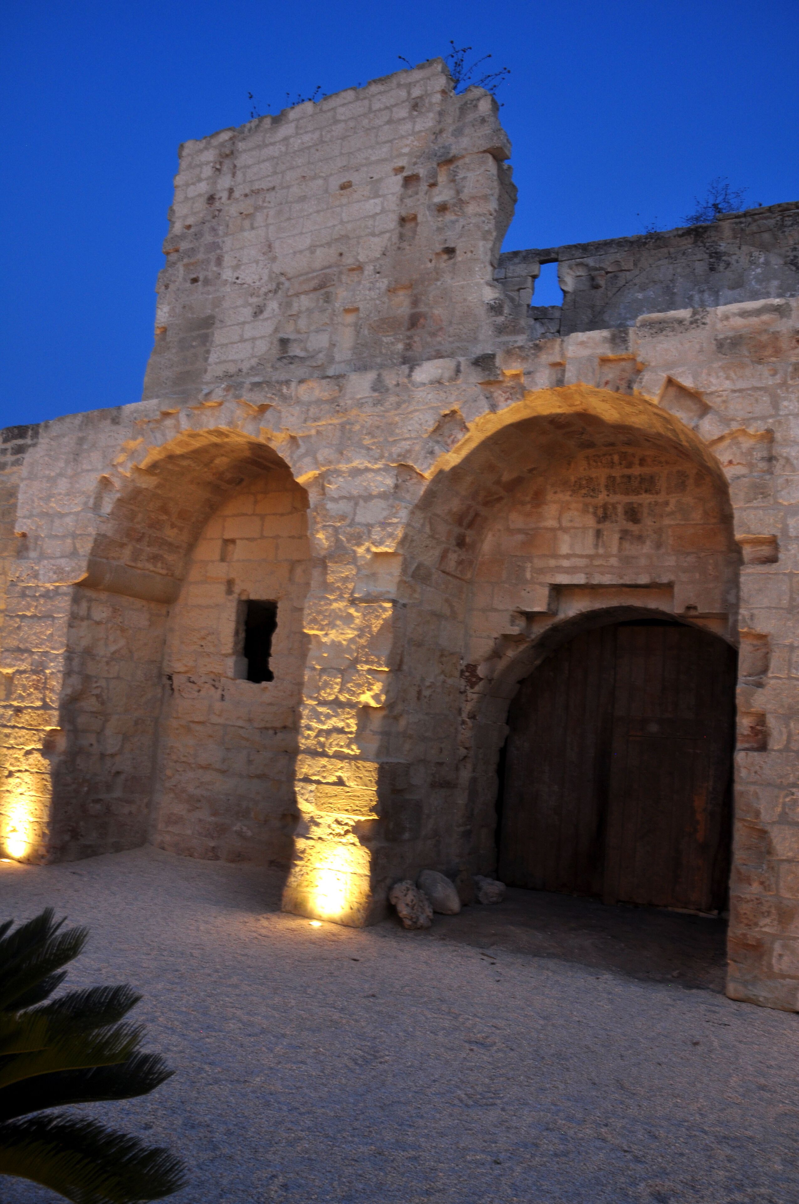 An ancient stone structure with two arched doorways and a large wooden door, illuminated by warm lighting.