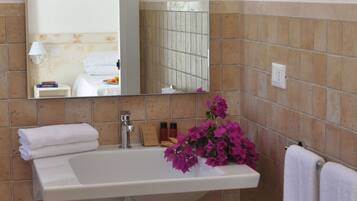 A bathroom with a white sink, a mirror, and a view of a coastal landscape.