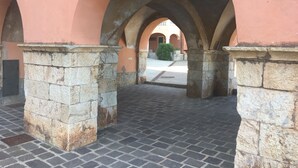 An architectural corridor with stone columns and arches, leading to a courtyard with a tiled floor. - Rio Marina studio apartment in a characteristic residence 10 meters from the sea (Rio Marina)