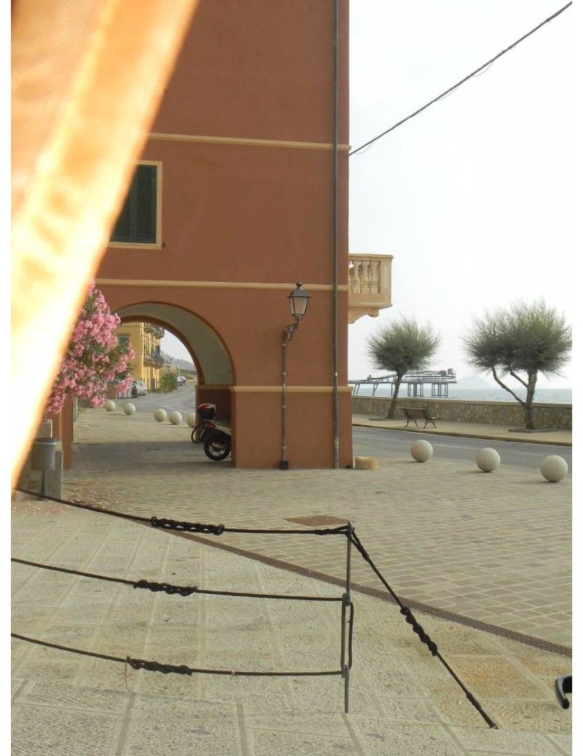 Un sendero pavimentado con una barandilla de metal, un edificio con un arco y un scooter estacionado.