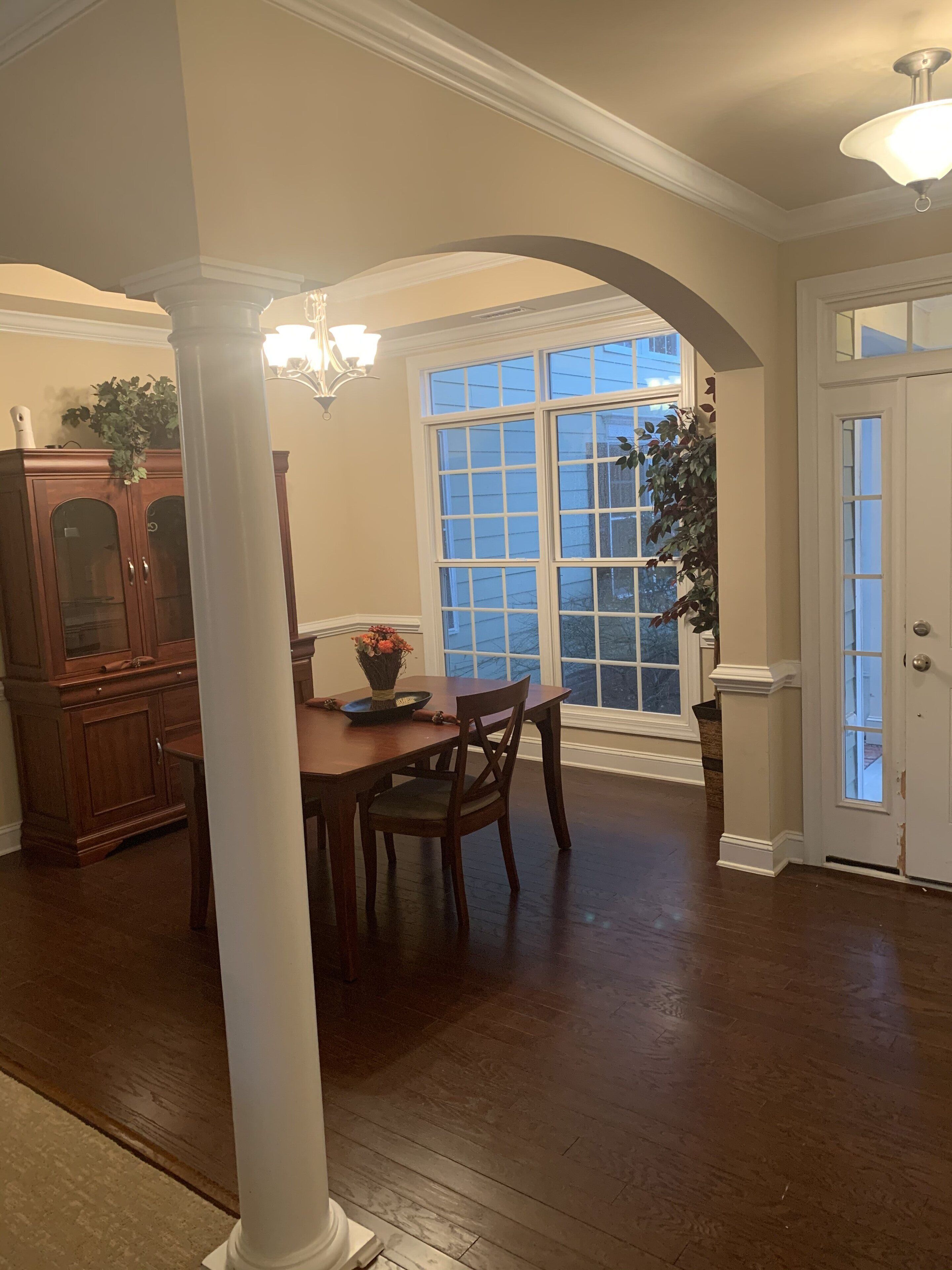 A dining area with a wooden table and chairs, a chandelier, and a large window with a view of the outside.