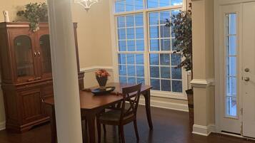 A dining area with a wooden table and chairs, a chandelier, and a large window with a view of the outside.