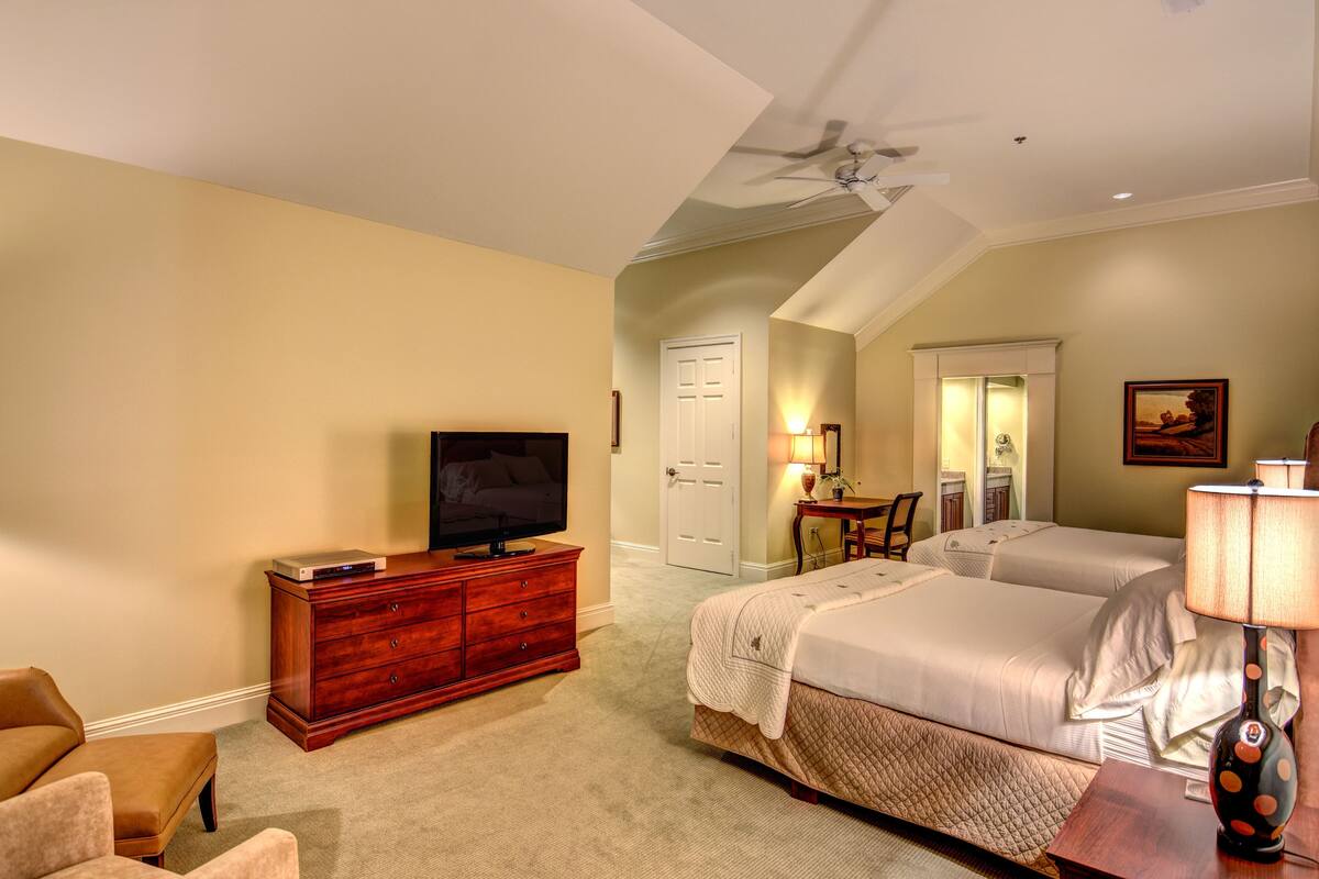 A hotel room with a large bed, a TV on a wooden dresser, a desk with a chair, and a ceiling fan.