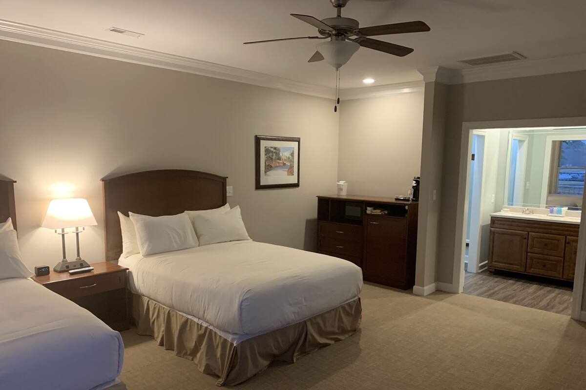 A hotel room with a bed, a nightstand with a lamp, a dresser, and a ceiling fan.