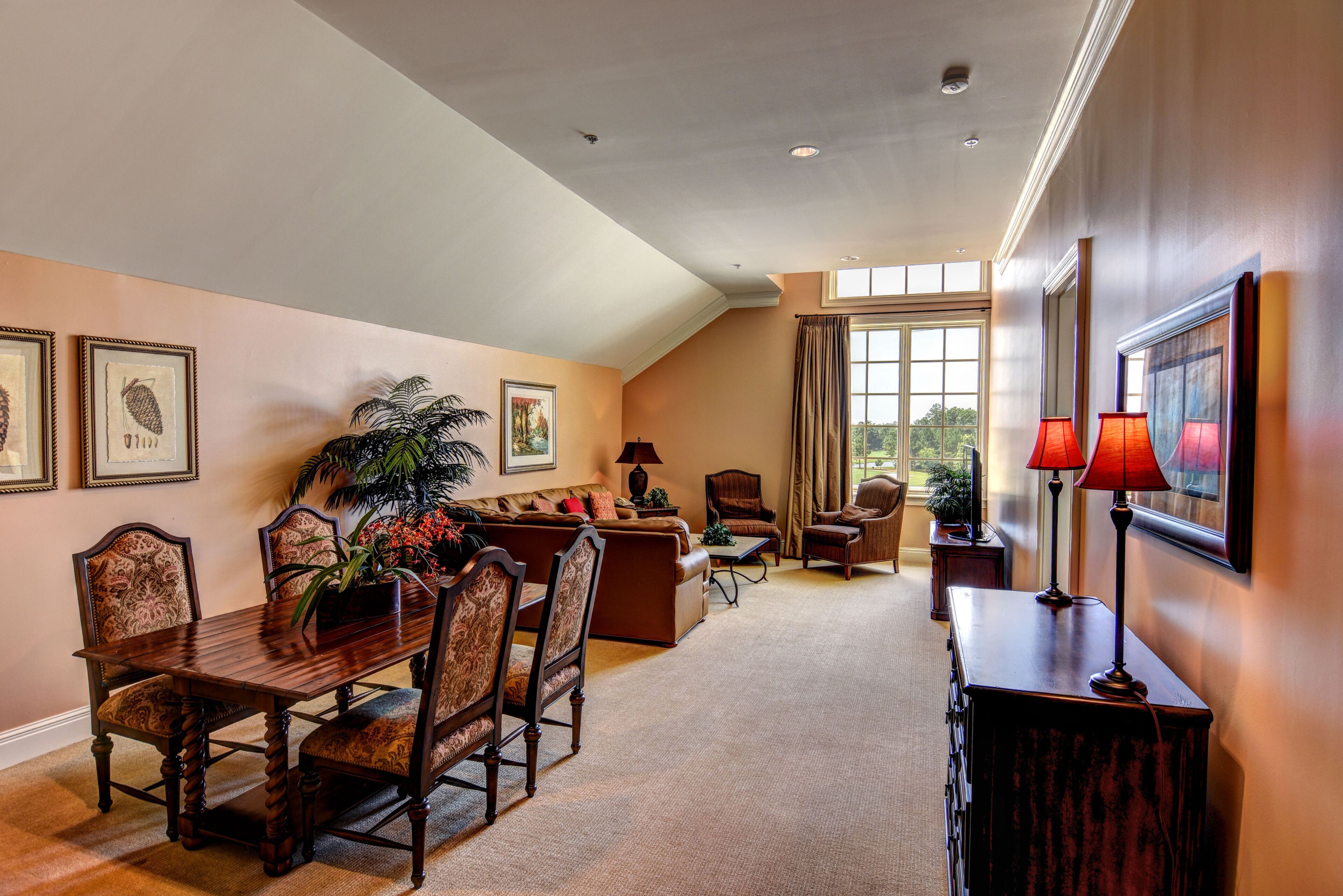 A spacious living room with a high ceiling, a dining area with a wooden table and chairs, and a large window providing natural light.