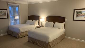 A hotel room with two beds, a ceiling fan, a window with blinds, and framed pictures on the walls.