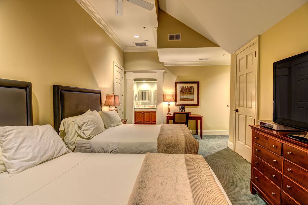 A hotel room with two beds, a dresser, a television, and a bathroom visible through an open door.